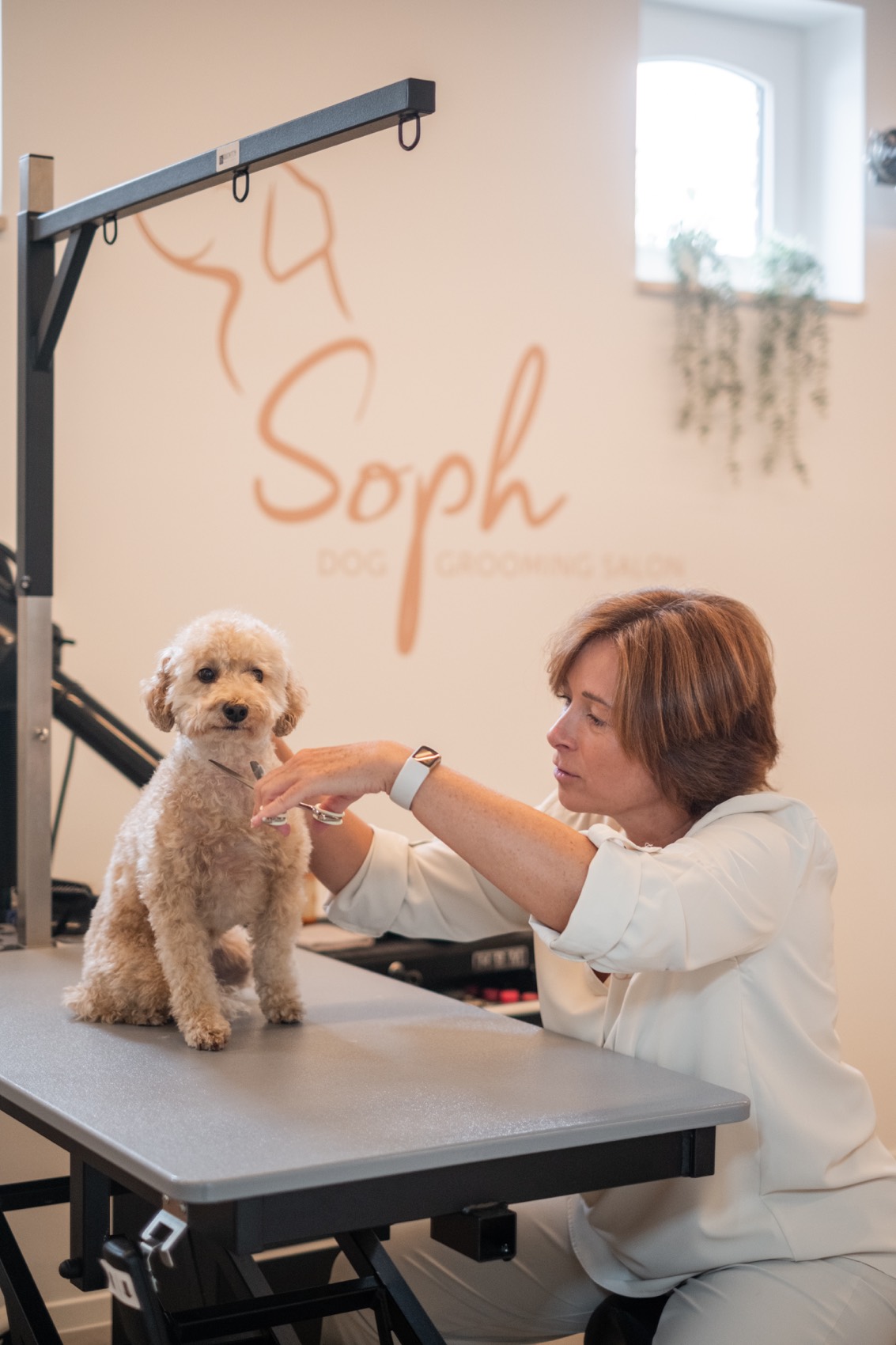Sophie zit rustig naast een hond in de trimsalon